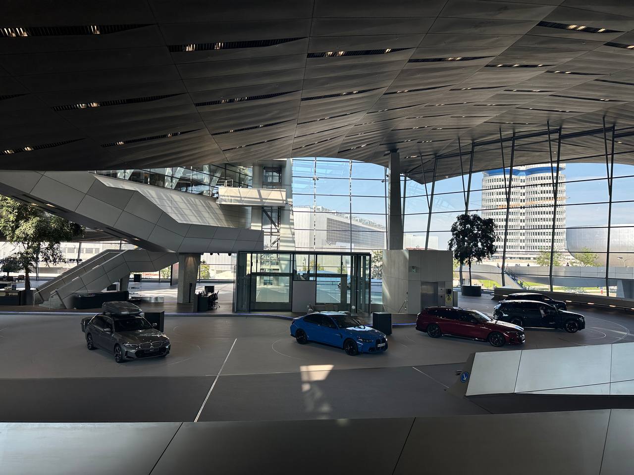The open interior of BMW Welt with modern BMW display cars and the headquarters tower visible outside.